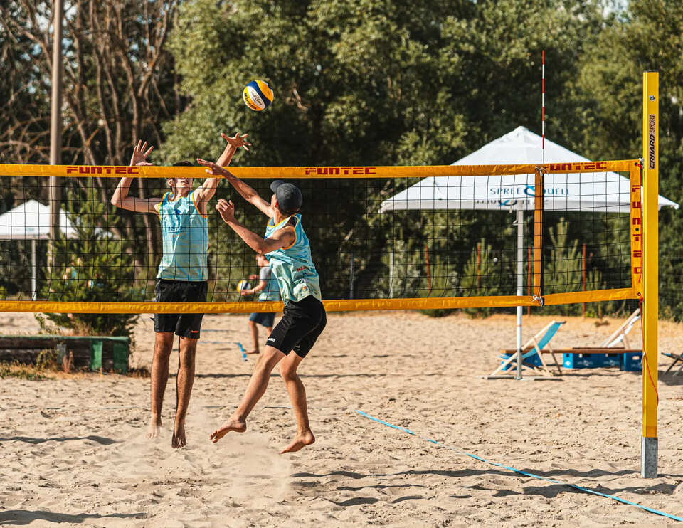 2 kleine Jungs sind am Netz und springen um den Ball